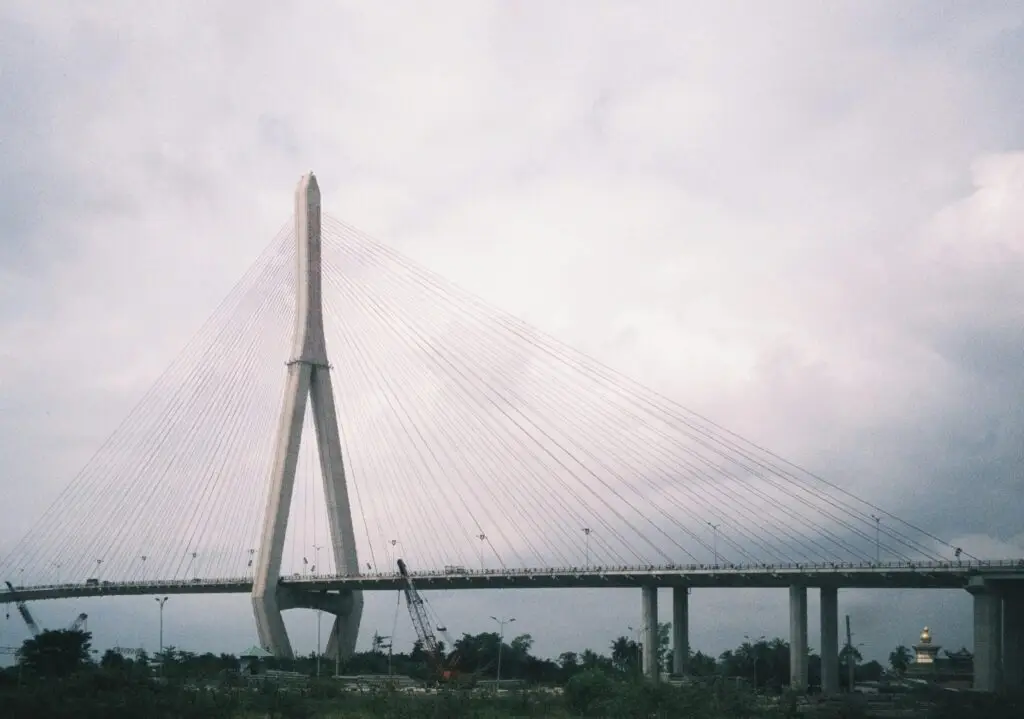 A dramatic view of a cable-stayed bridge in Cần Thơ, Vietnam against a cloudy sky.